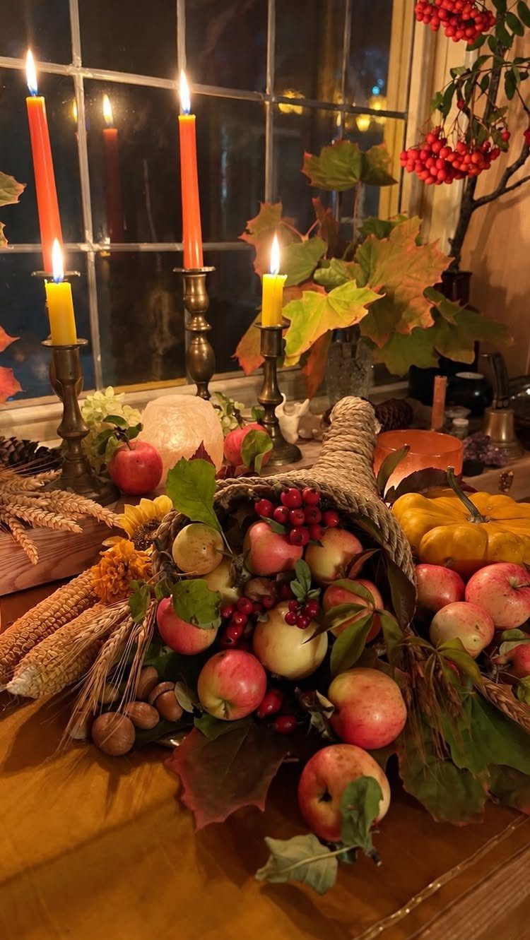 Woven cornucopia overflowing with red apples and autumn leaves beside lit taper candles.