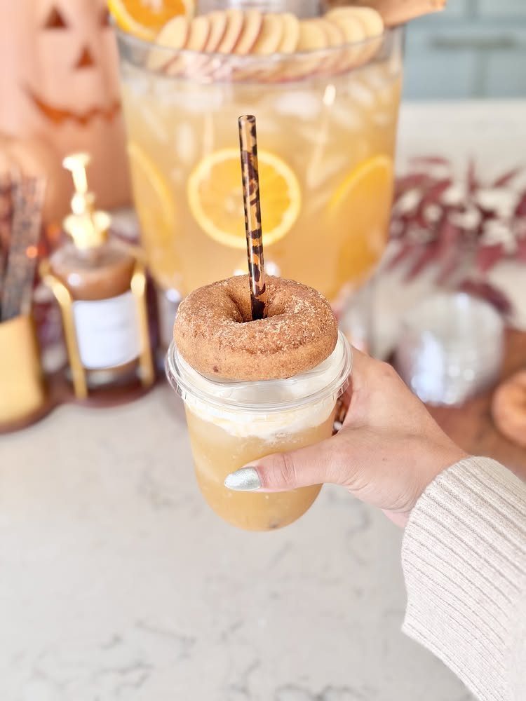 Iced orange drink topped with a cinnamon donut held in front of beverage station
