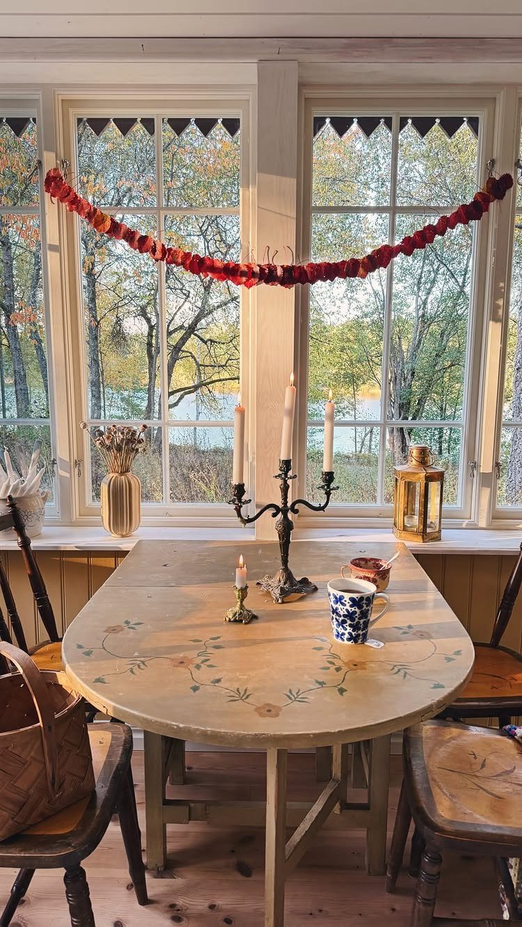 Red leaf garland draped across windows above a rustic dining table with candles.