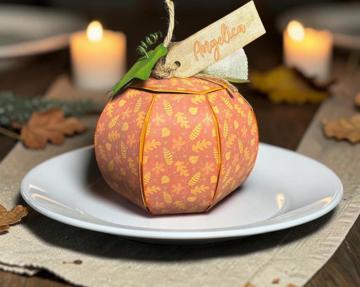 Paper pumpkin place card with a name tag on a white dinner plate.