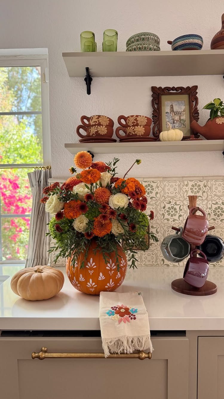 Pumpkin-shaped vase filled with autumn flowers on a white kitchen counter.