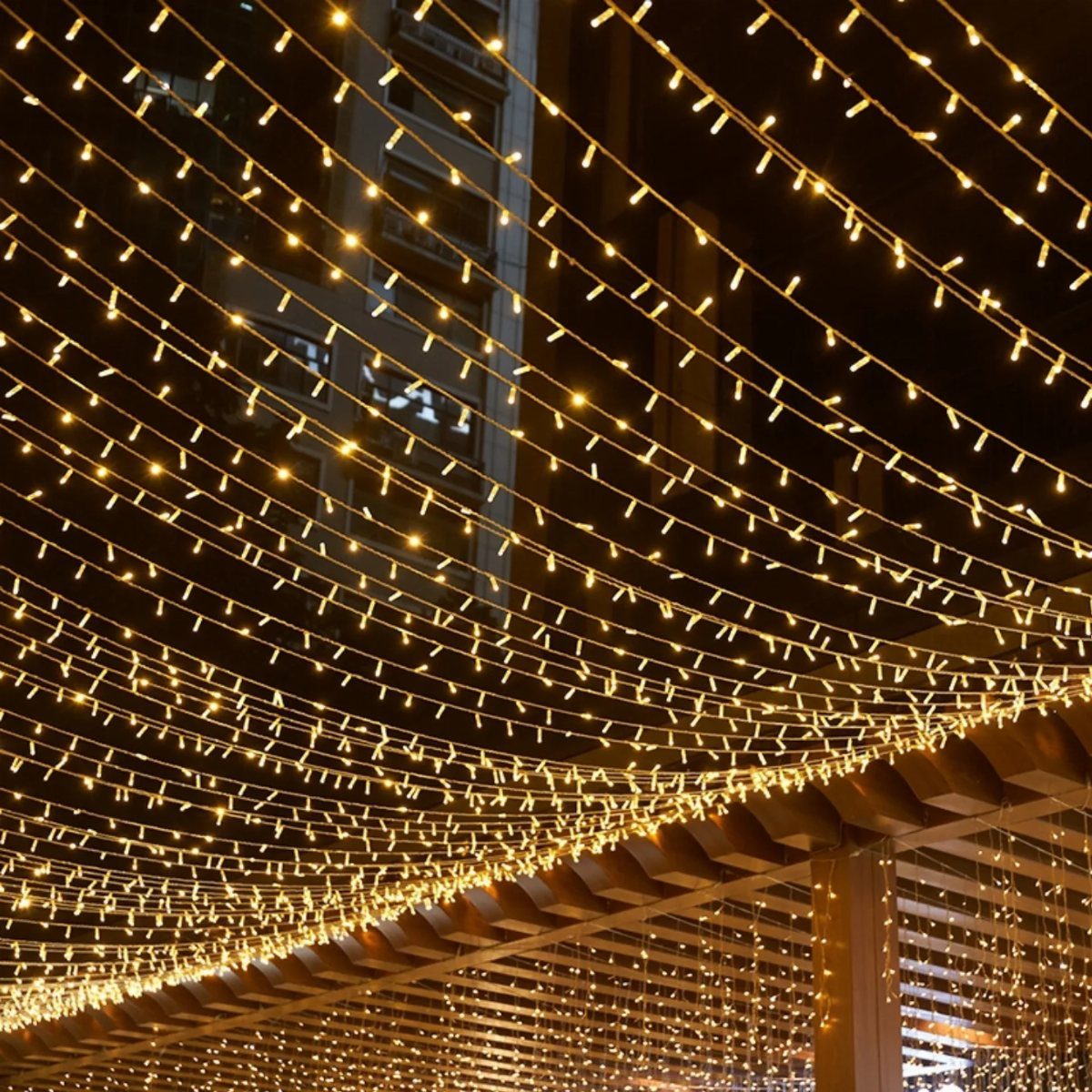 Warm yellow string lights forming a glowing canopy over an outdoor wooden structure.
