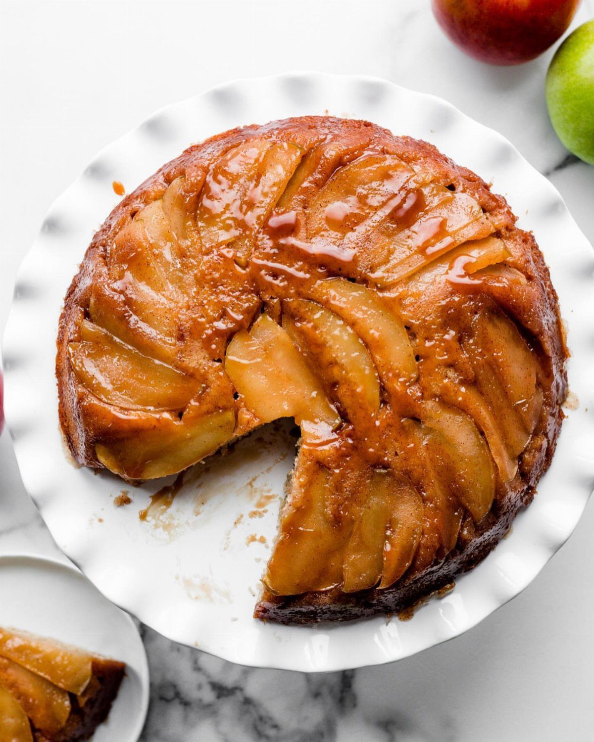 Caramelized apple upside-down cake on a white scalloped plate with a slice removed.
