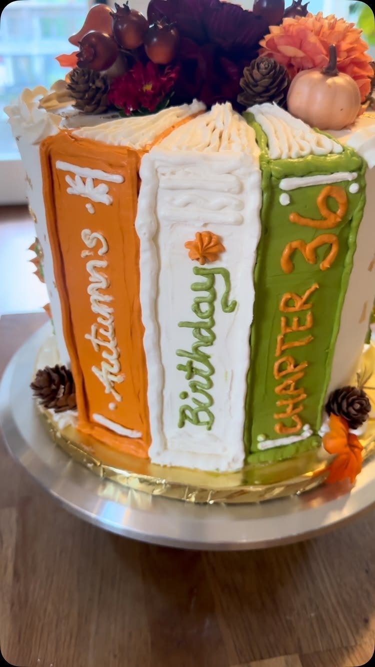Autumn themed birthday cake shaped like books with pumpkins and pinecones on top.