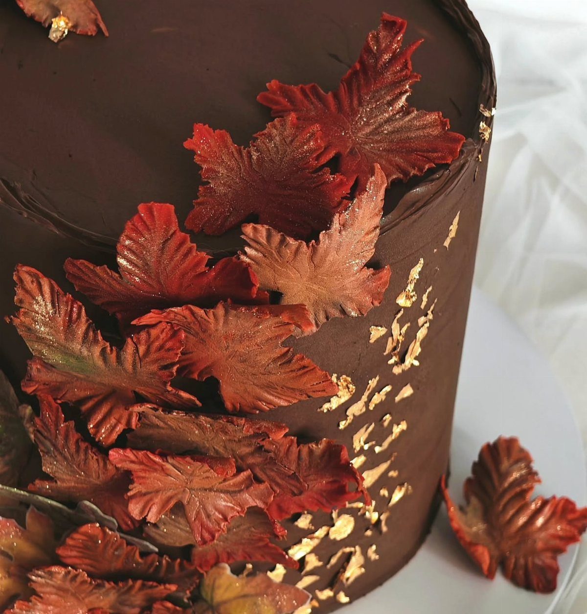 Chocolate frosted cake decorated with red autumn leaves and gold leaf accents.
