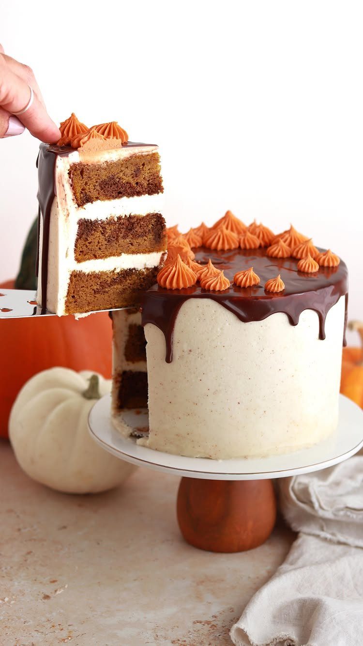 Layered chocolate pumpkin cake with chocolate drip and orange frosting on a stand.