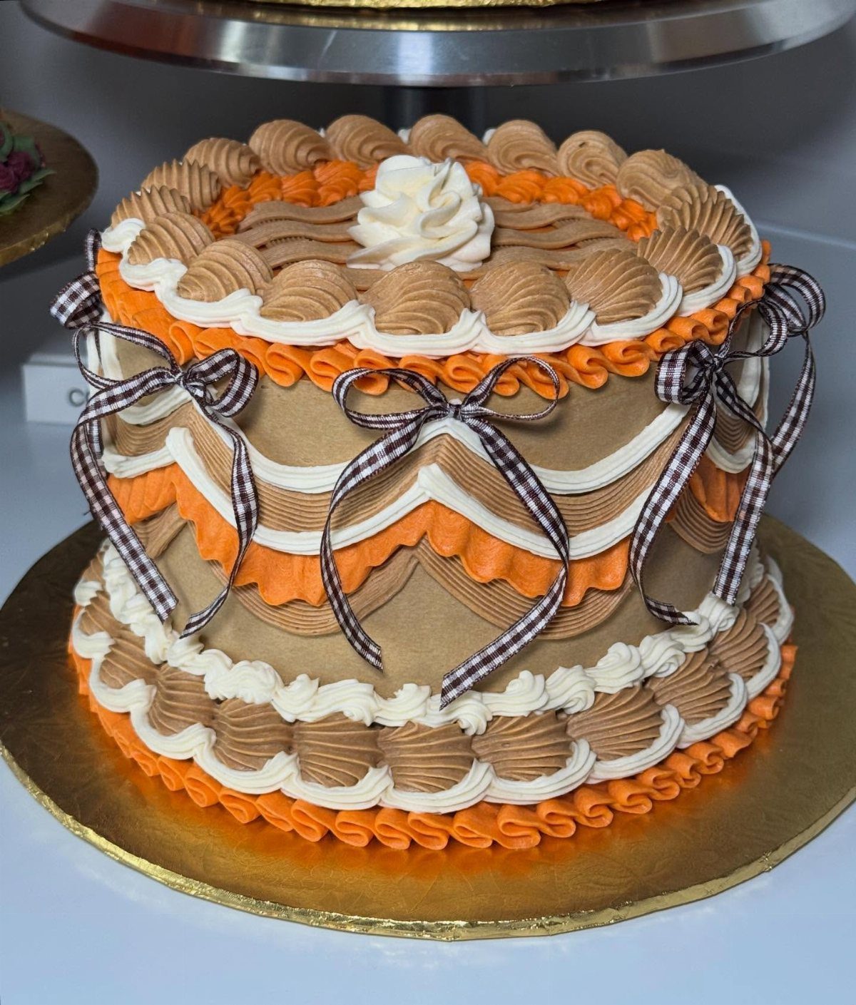 Fall themed cake with orange and brown frosting and checkered ribbon bows.