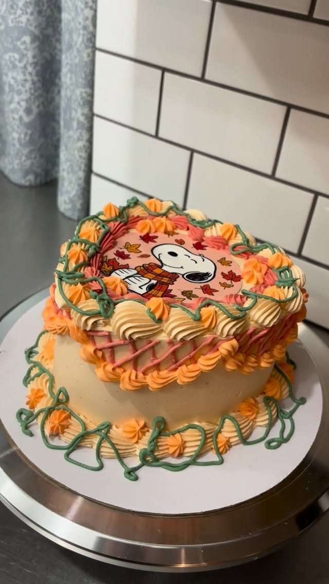 Layer cake with orange frosting and a Snoopy autumn leaf edible image topper.