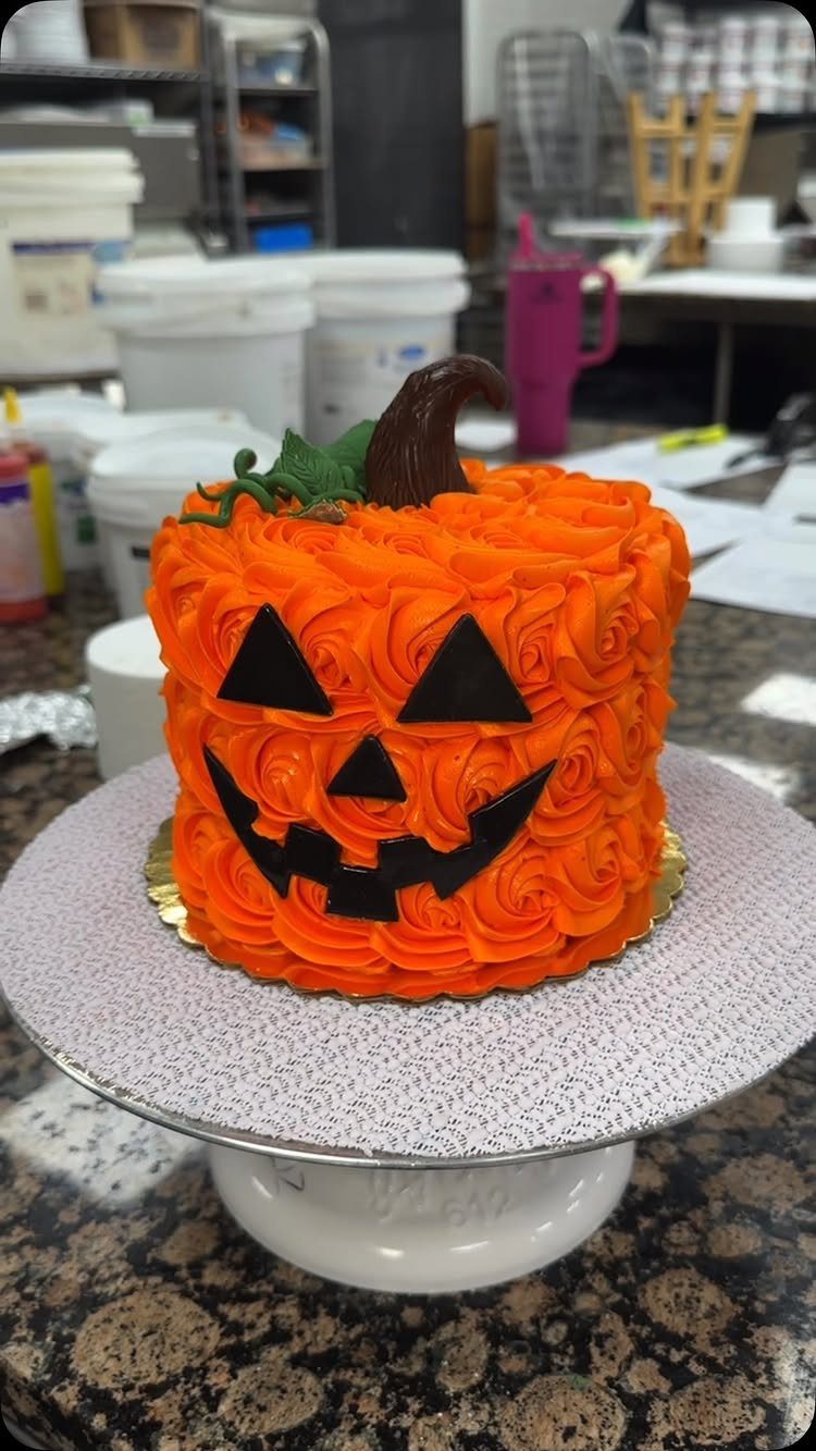 Jack-o'-lantern cake with orange rosette frosting and black facial features on a stand.