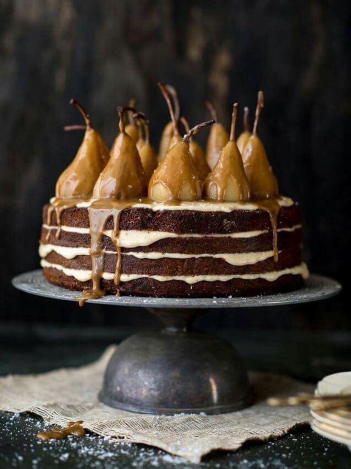 Layered dark brown cake topped with glazed pears and dripping caramel sauce.