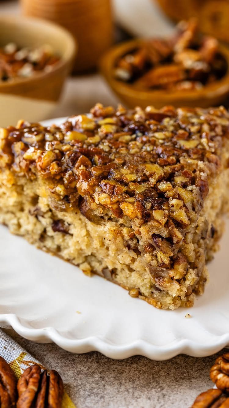 Slice of cake topped with glazed pecans on a white scalloped plate.