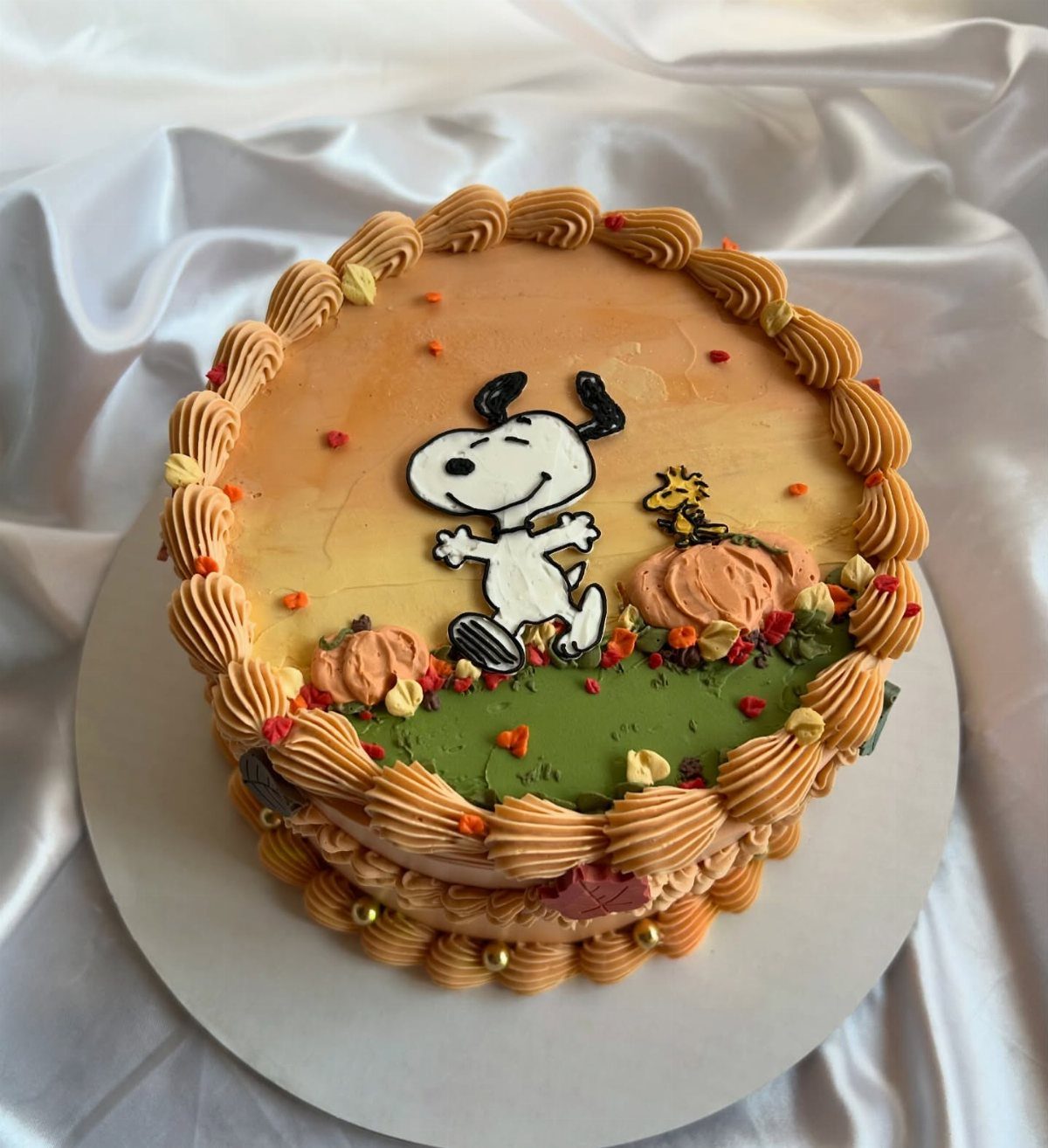 Snoopy cake with orange frosting, pumpkins, and autumn colors on white satin.