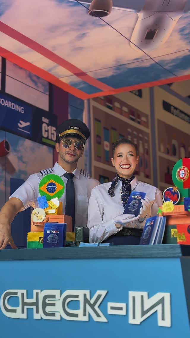 Pilot and flight attendant posing behind a blue airport check-in counter with travel props.