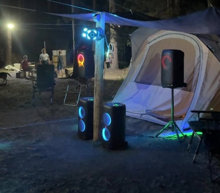 Outdoor camping setup with large glowing speakers and disco lights near a tent.