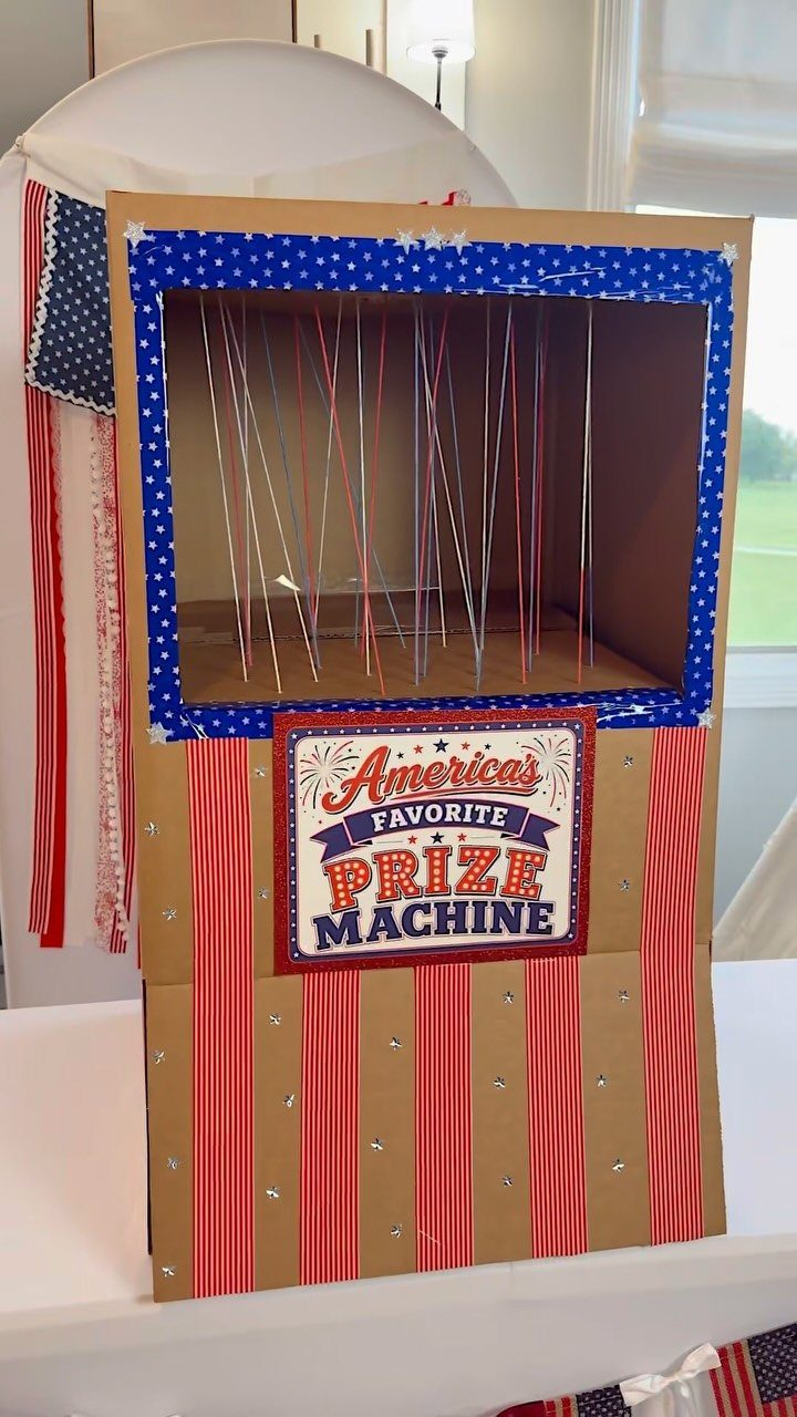 Homemade cardboard prize machine with red white and blue patriotic decorations and strings.