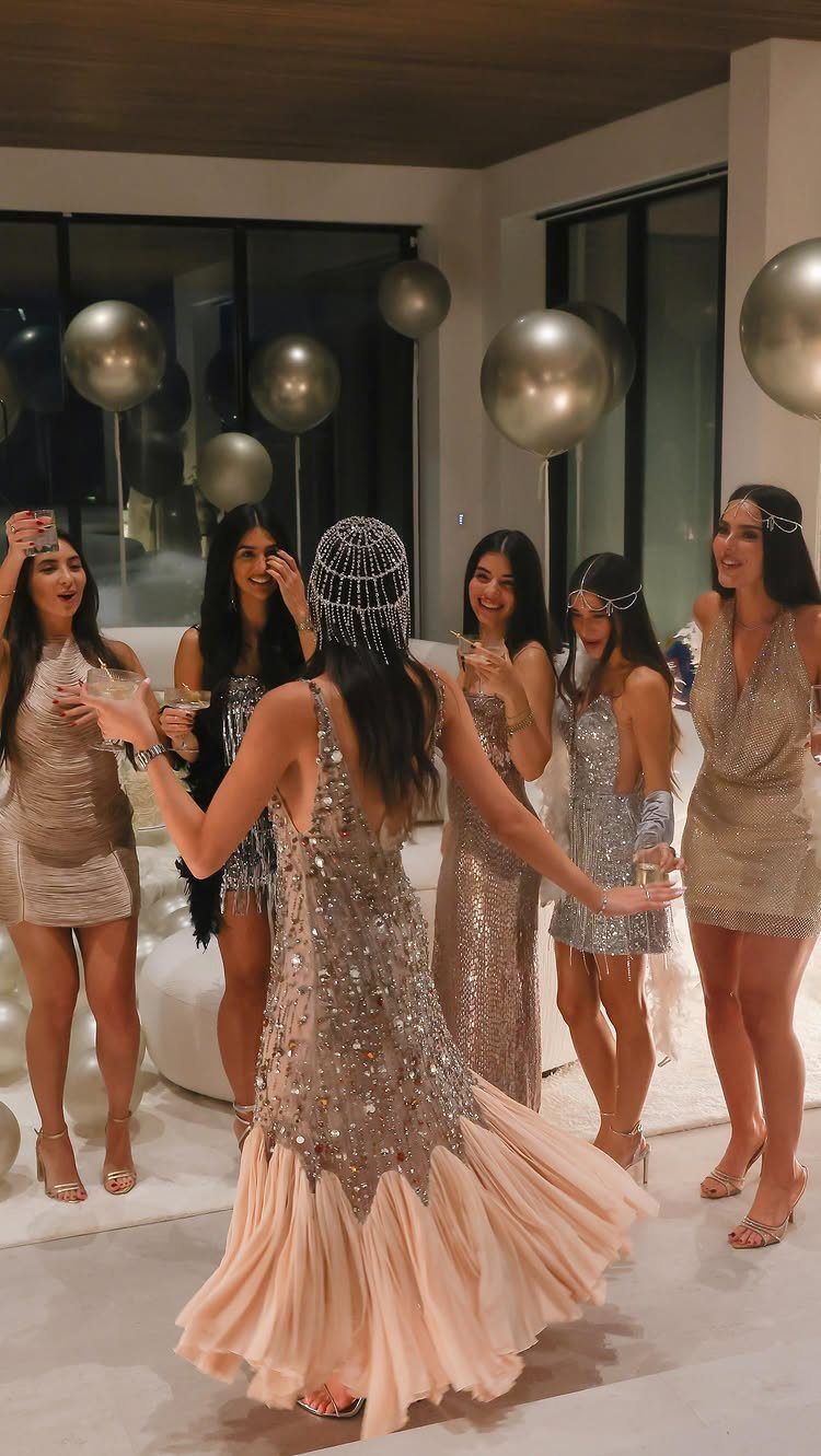 Women in sequined flapper dresses and headbands holding cocktails at a party.