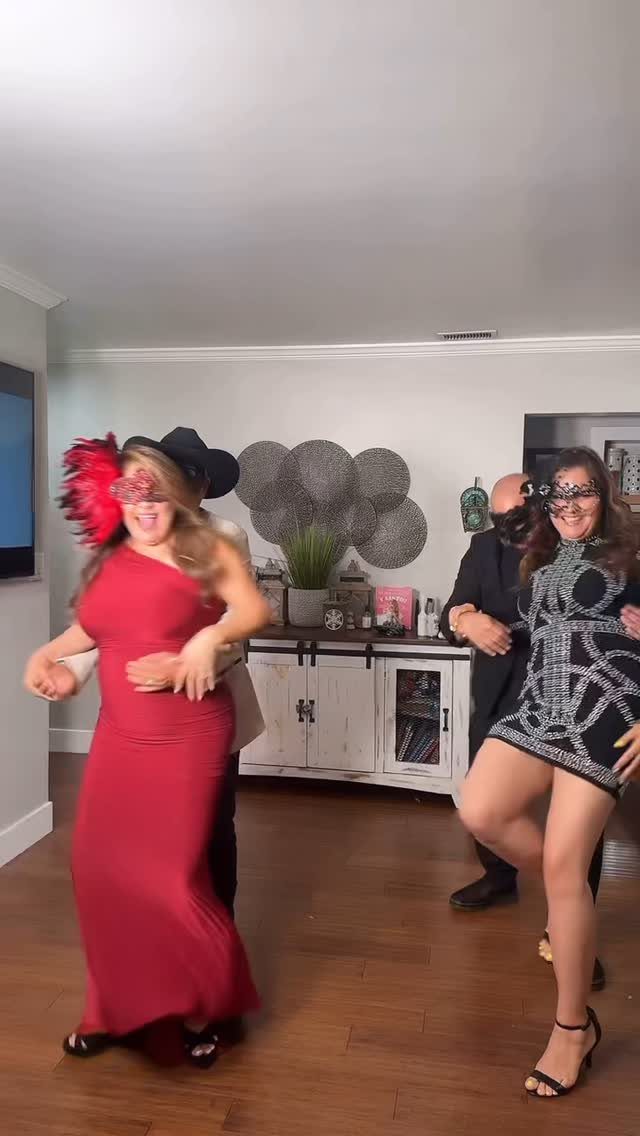 People wearing formal dresses and suits with masquerade masks in a living room.
