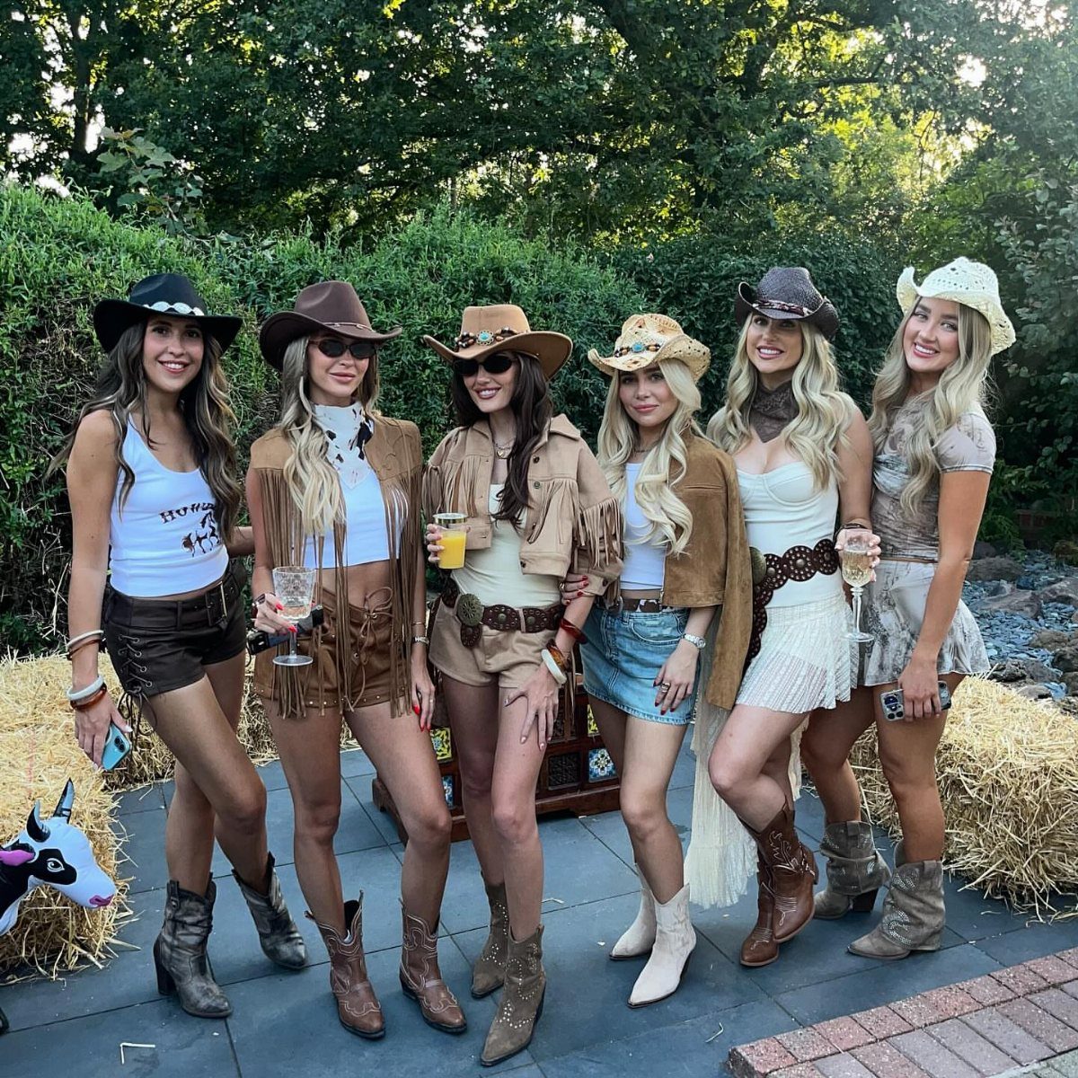 Six women in cowboy hats and boots posing at a Western themed party.