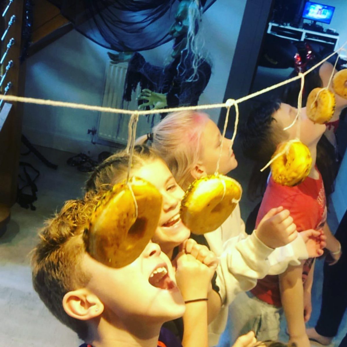 Children trying to eat glazed doughnuts hanging from a string without using hands.
