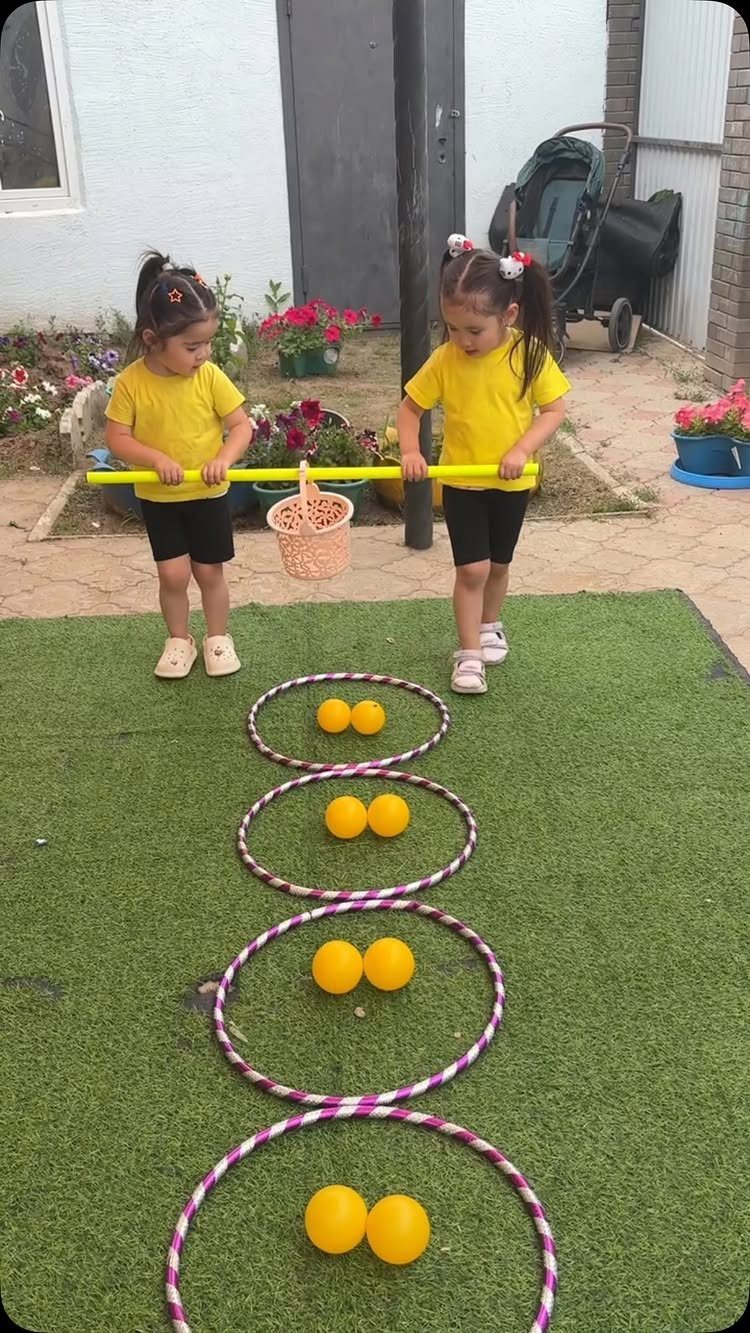 Two girls in yellow shirts playing a coordination game with hula hoops and balls.