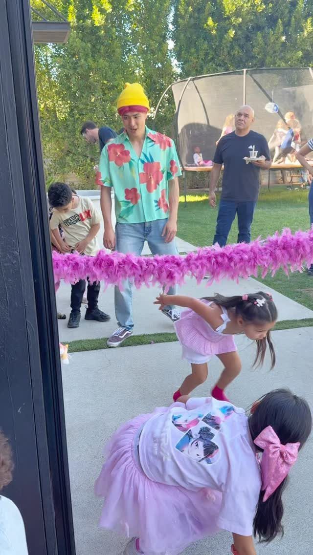 Children leaning back to pass under a pink feather boa during a limbo game.