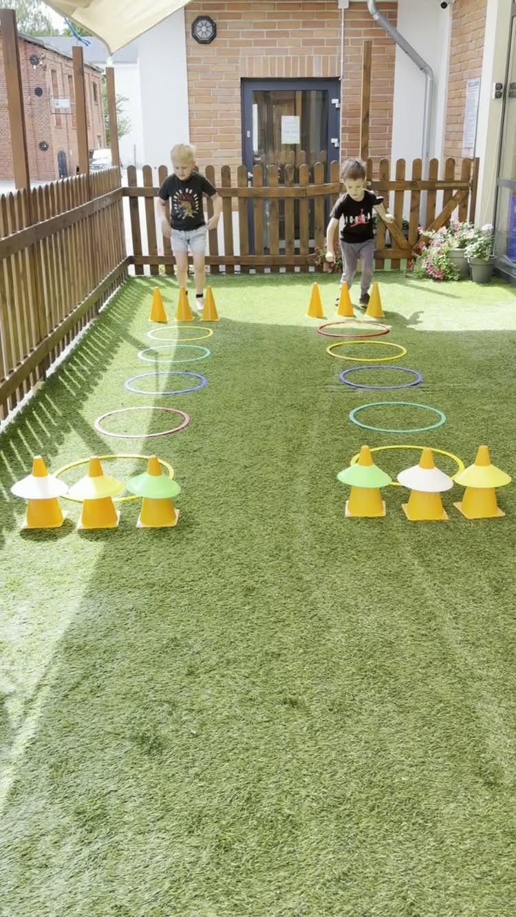 Two children standing at the start of a backyard obstacle course with hoops and cones.