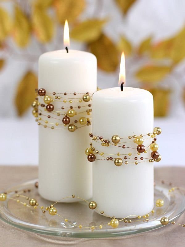 Two white pillar candles wrapped in gold beaded garlands on a glass plate.