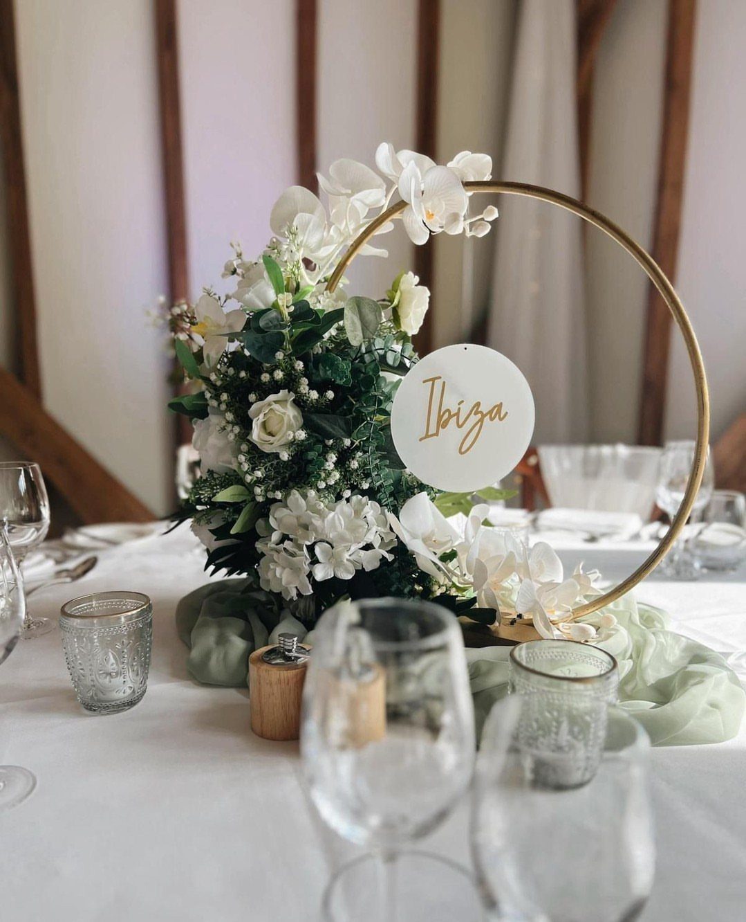 Gold metal hoop centerpiece with white orchids and greenery on a wedding table