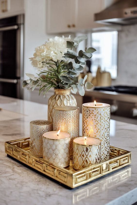 Gold decorative tray with patterned candles and white flowers on marble countertop