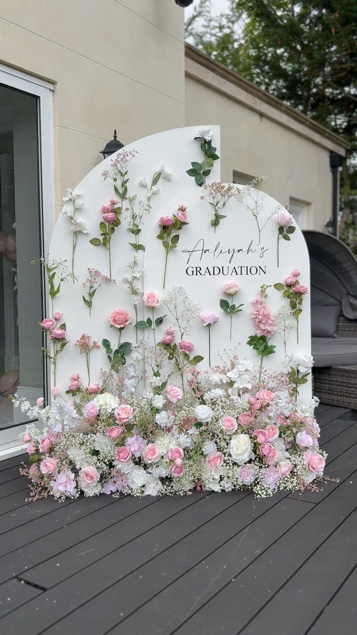 White arched graduation backdrop decorated with pink and white roses on a deck