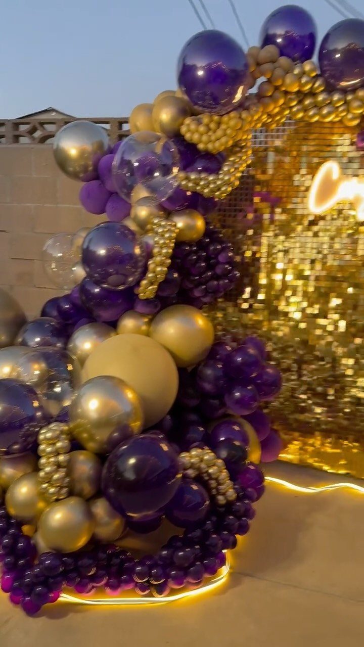 Gold sequin shimmer wall backdrop with a purple and gold balloon arch.