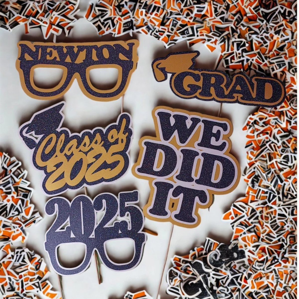 Graduation photo booth props with glittery text and caps on a confetti background.