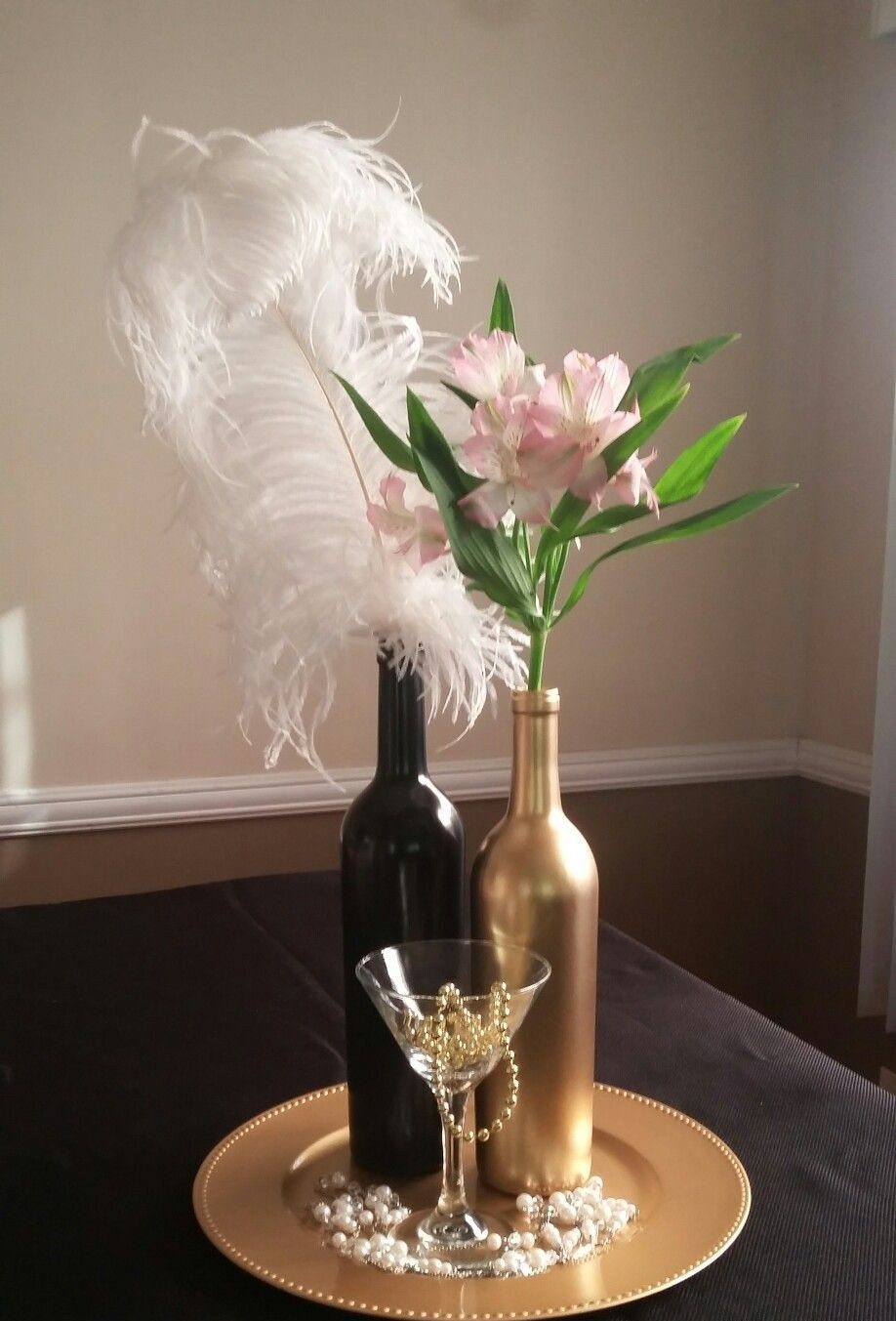 Black and gold painted bottles with white feathers and pink lilies on gold tray