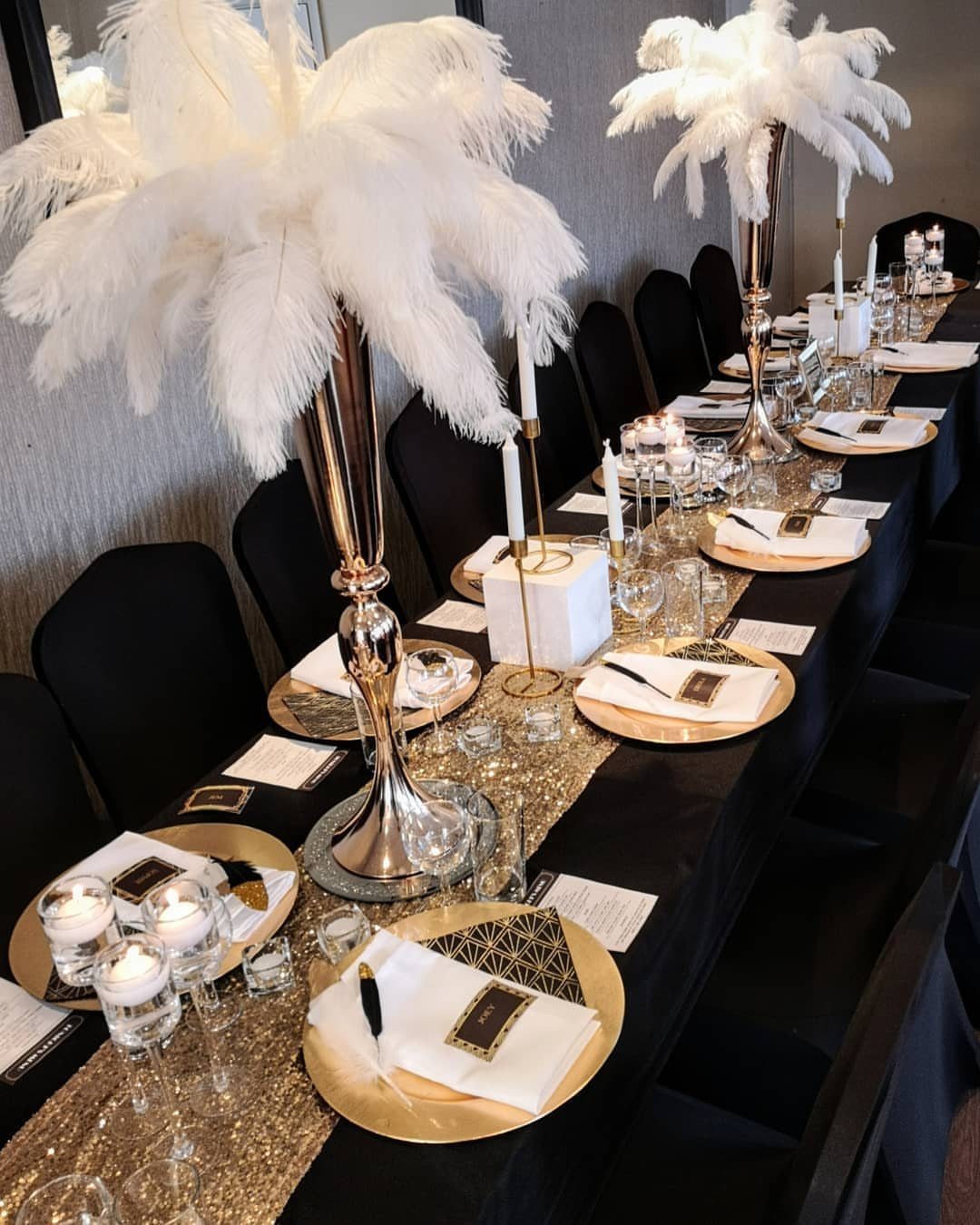 Tall gold vases with white ostrich feathers on a black and gold table.