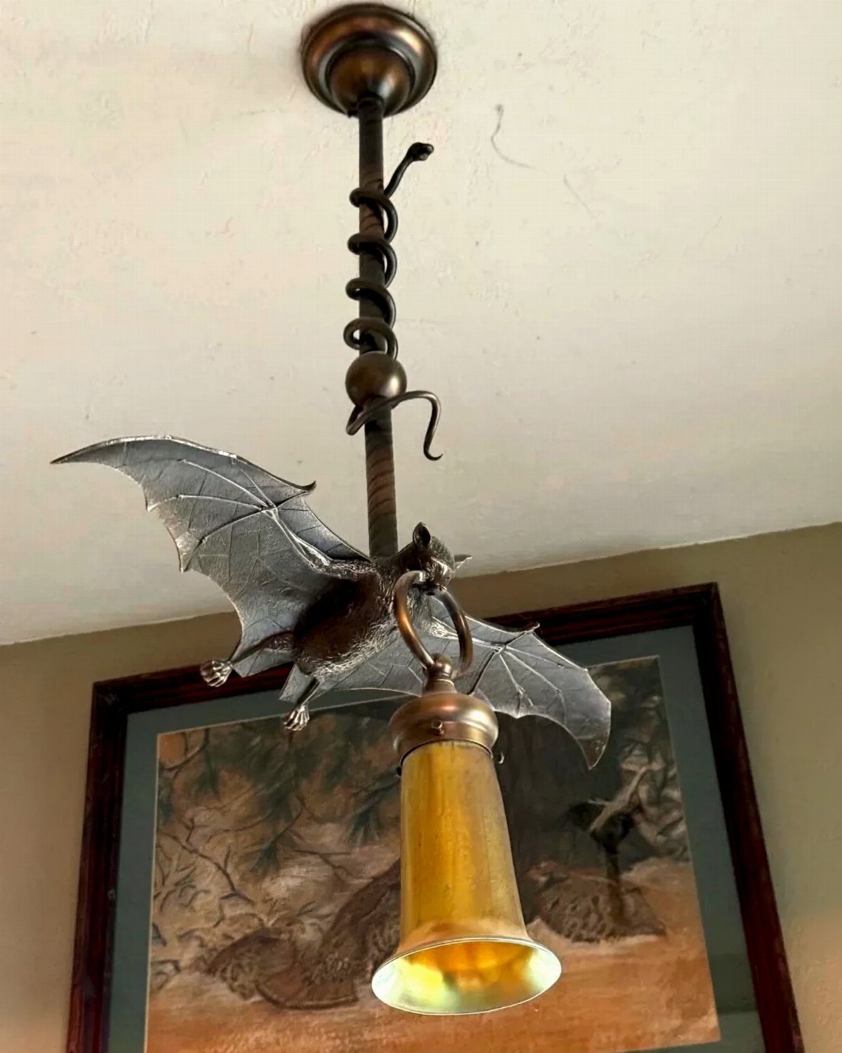 Bronze bat ceiling light fixture with outstretched wings and a glowing yellow lampshade.