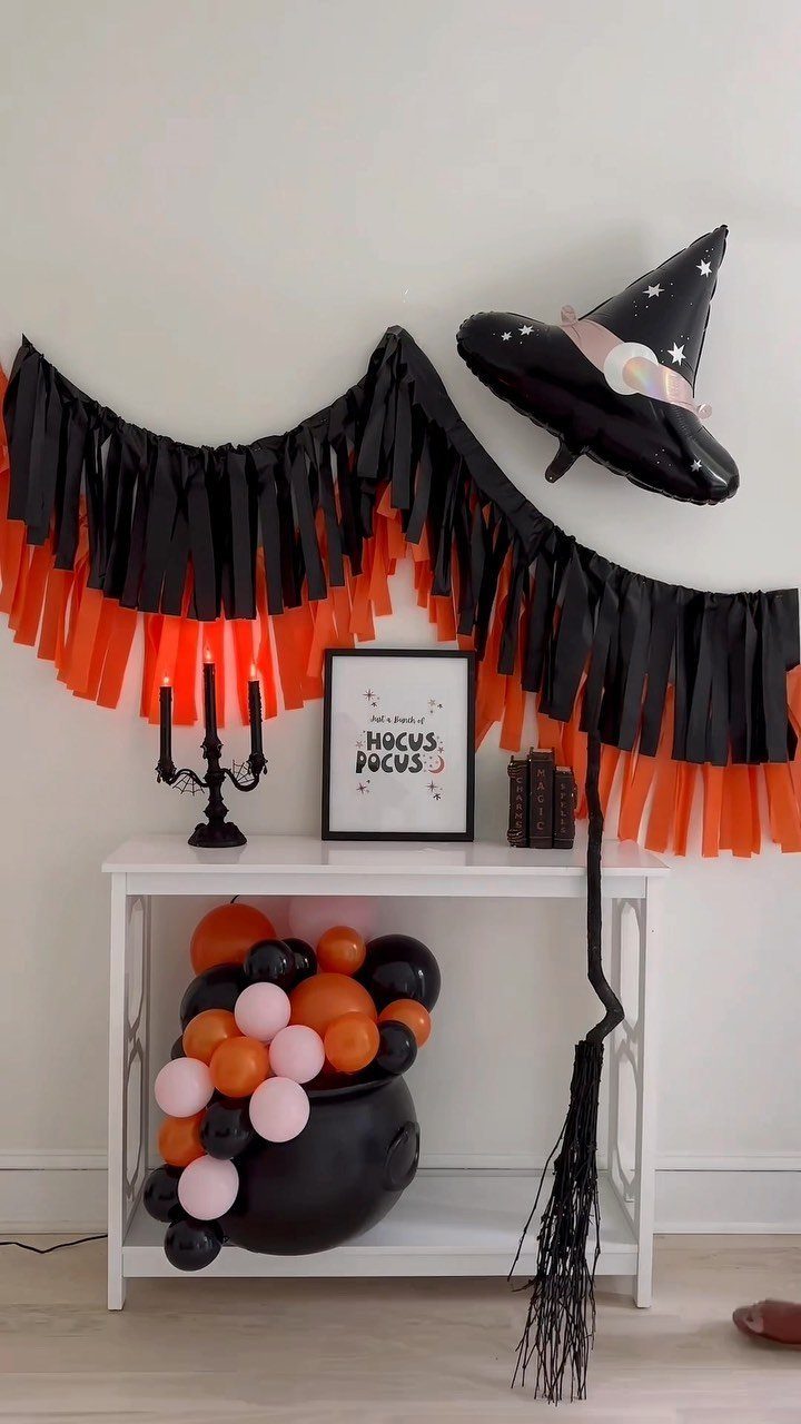 White table with a balloon cauldron, orange and black fringe banner, and witch hat.