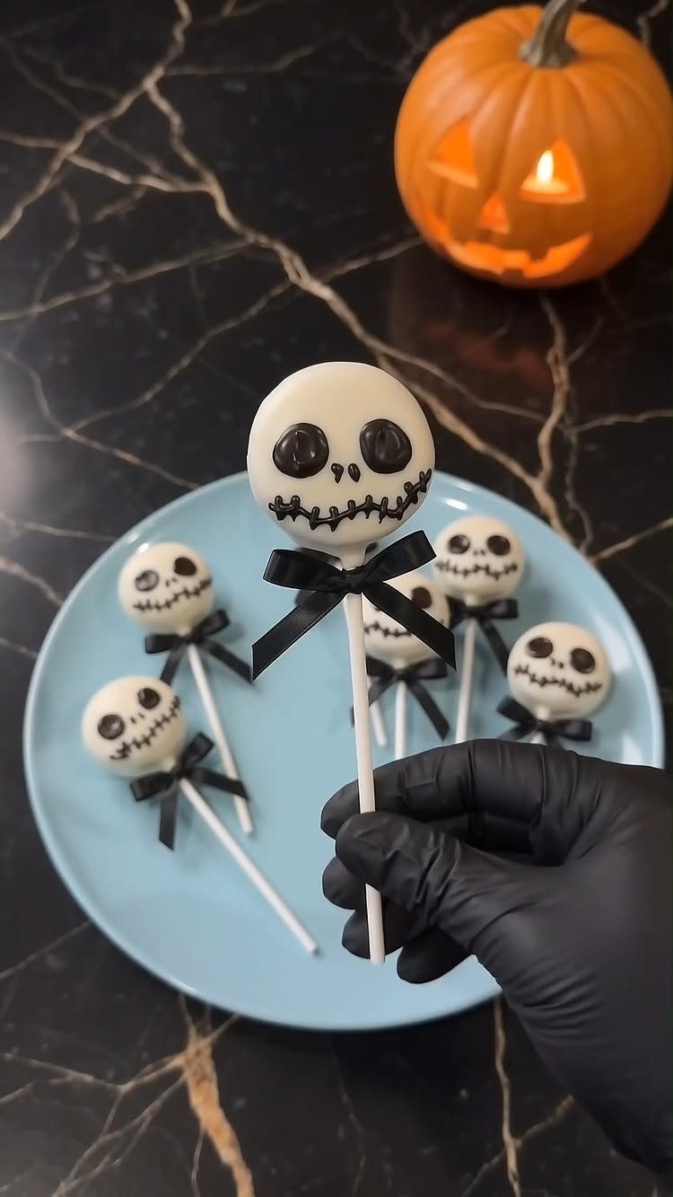 Skeleton skull cake pops on a blue plate with a glowing pumpkin background