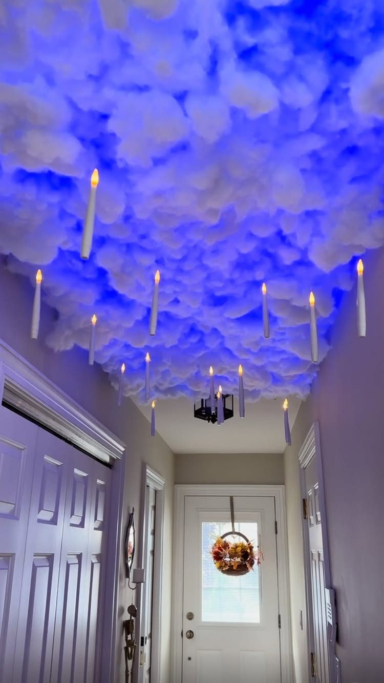 Floating white candles hanging from a blue illuminated cloud ceiling in a hallway.
