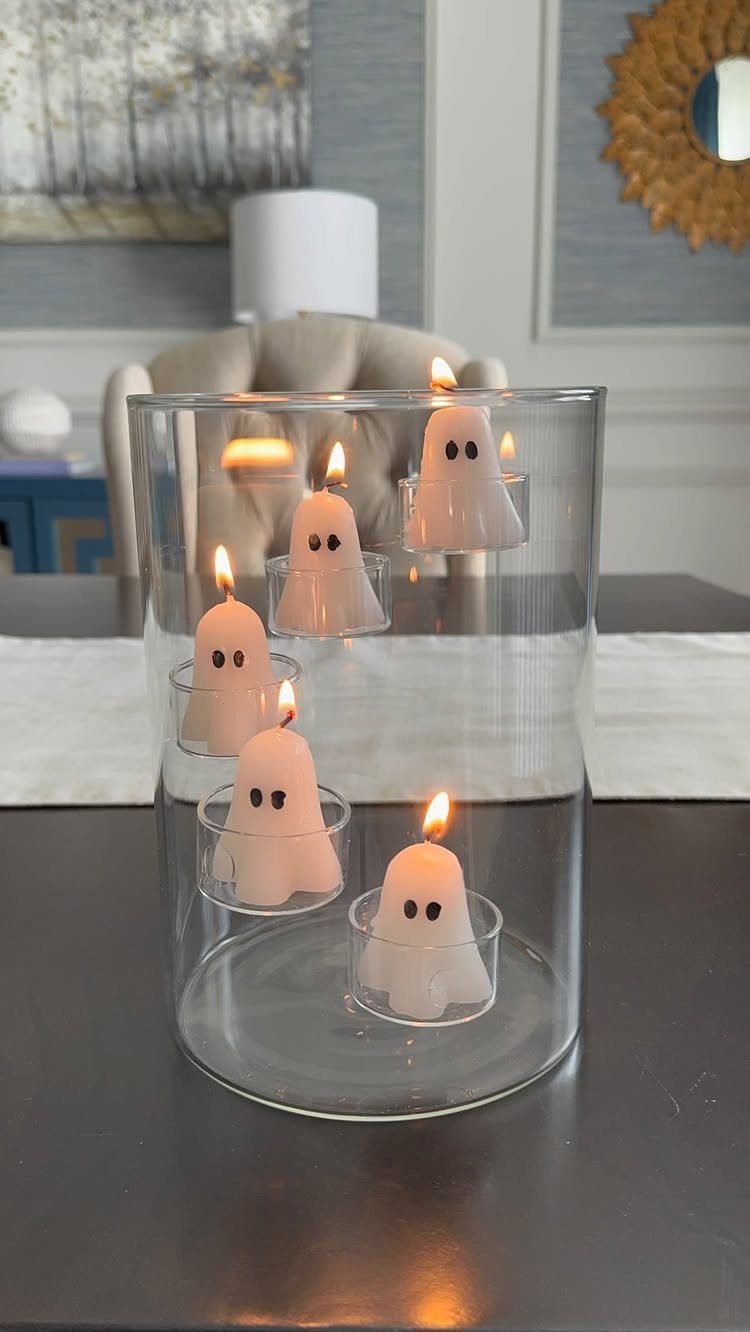 Ghost-shaped tea light candles lit inside a clear glass cylinder on a table.