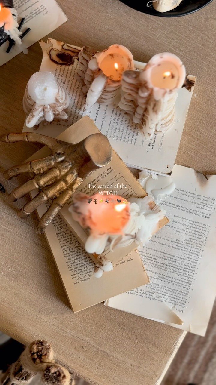 Skeletal rib and skull candles lit atop vintage books with a golden skeletal hand.