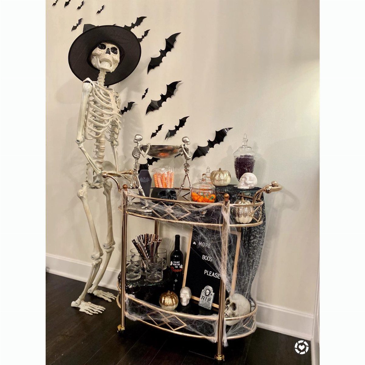 Gold bar cart with Halloween decorations and a skeleton wearing a witch hat