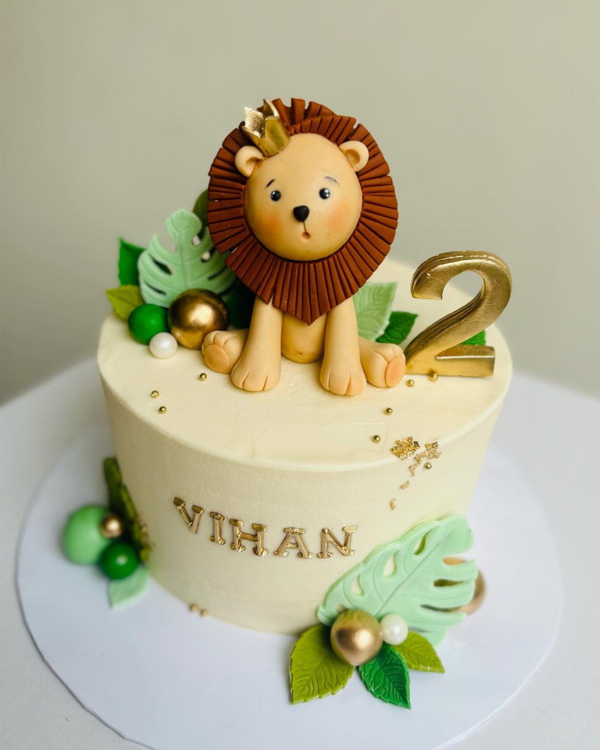 Cream cake topped with a 3D fondant lion, gold number 2, and tropical leaves.