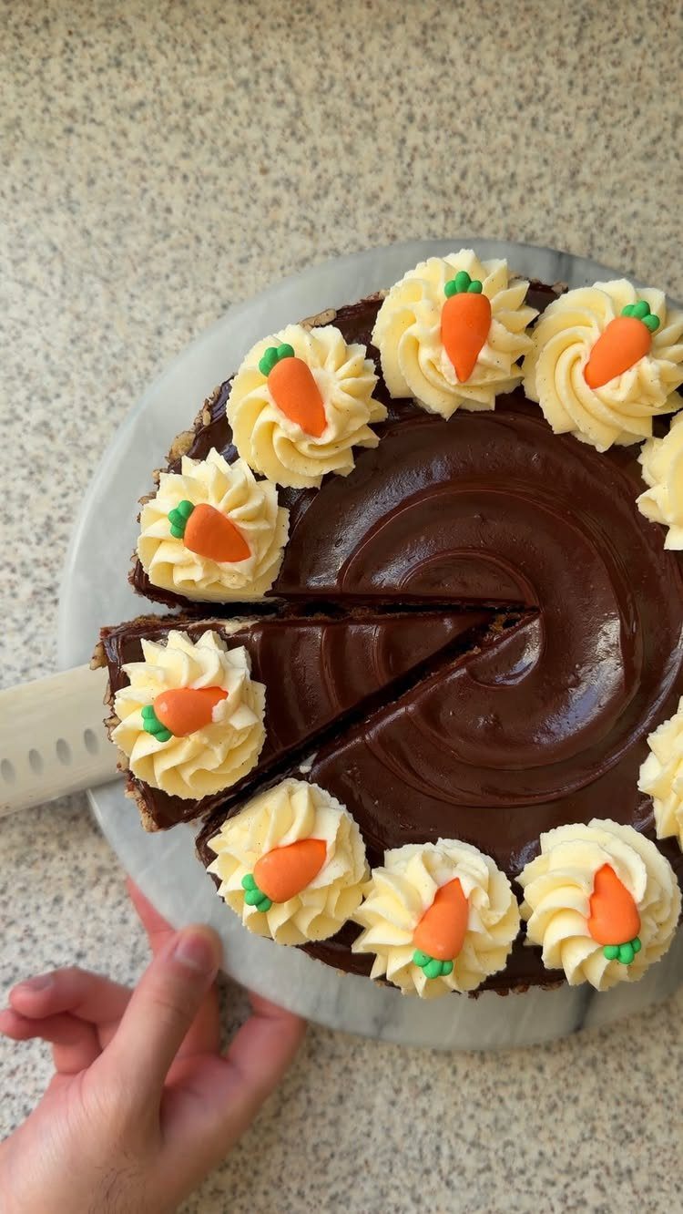 Chocolate frosted cake decorated with white buttercream swirls and tiny orange carrot candies.