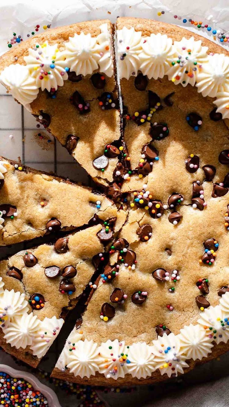 Chocolate chip cookie cake with white frosting swirls and colorful rainbow sprinkles.