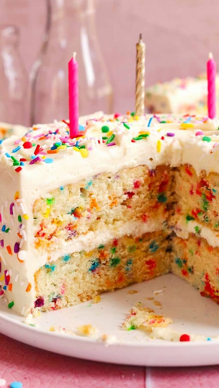 Two-layer white frosted cake with colorful sprinkles inside and out and birthday candles.