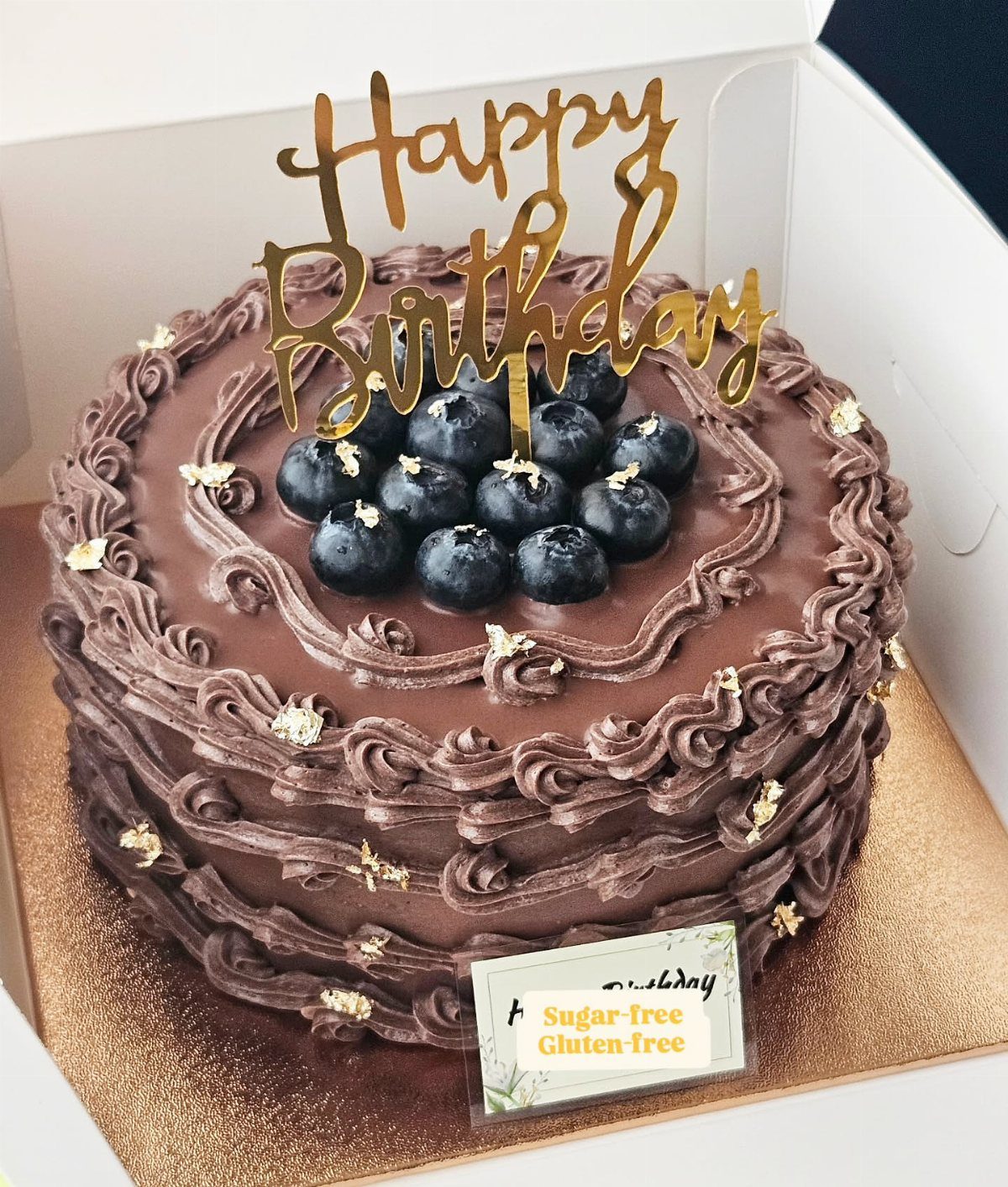 Chocolate birthday cake topped with blueberries and a gold Happy Birthday topper.