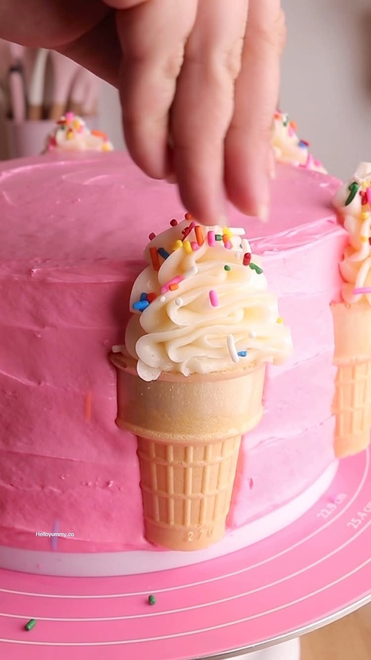 Ice cream cone with white frosting attached to a pink frosted birthday cake.