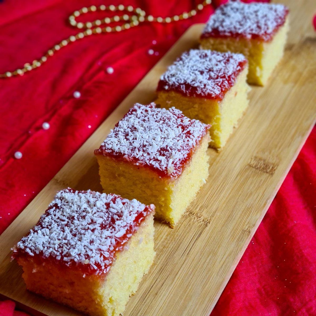 Four slices of yellow sponge cake topped with red jam and shredded coconut.