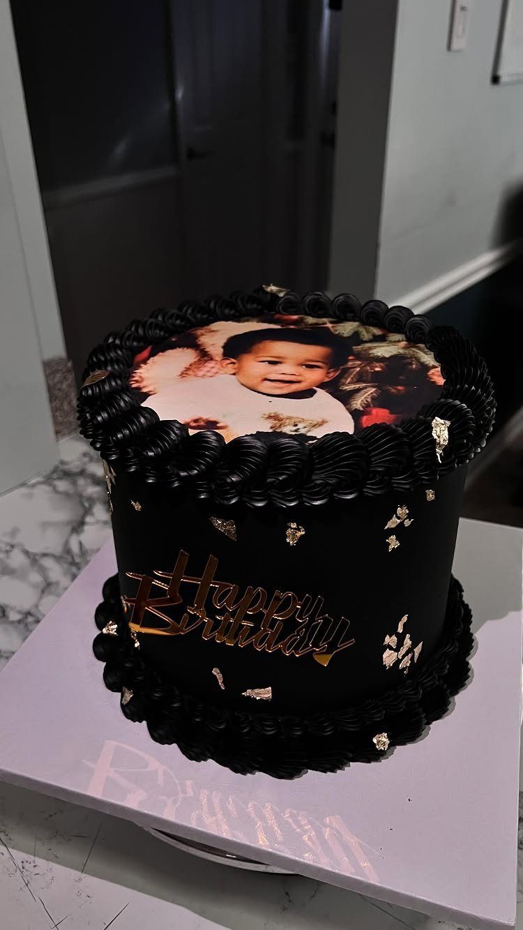 Black birthday cake with an edible photo of a baby and gold lettering.