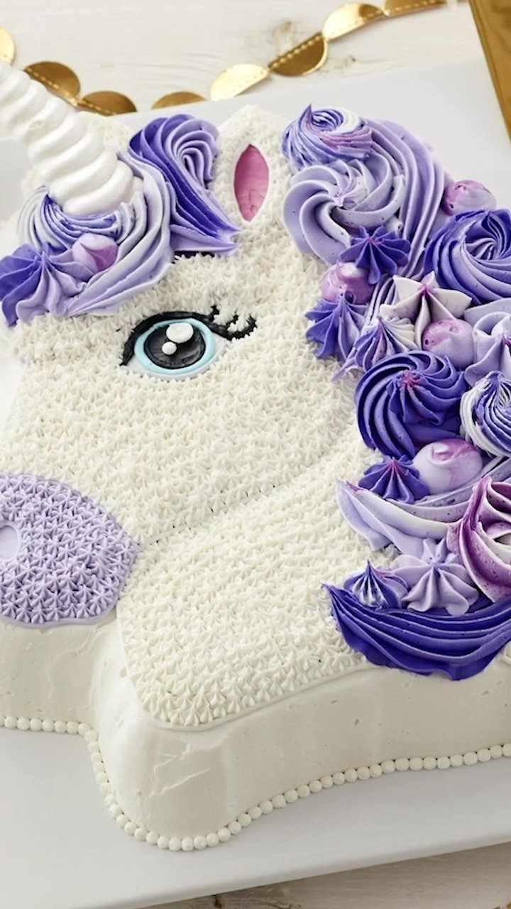 Unicorn head cake with purple buttercream mane and a white horn on white background